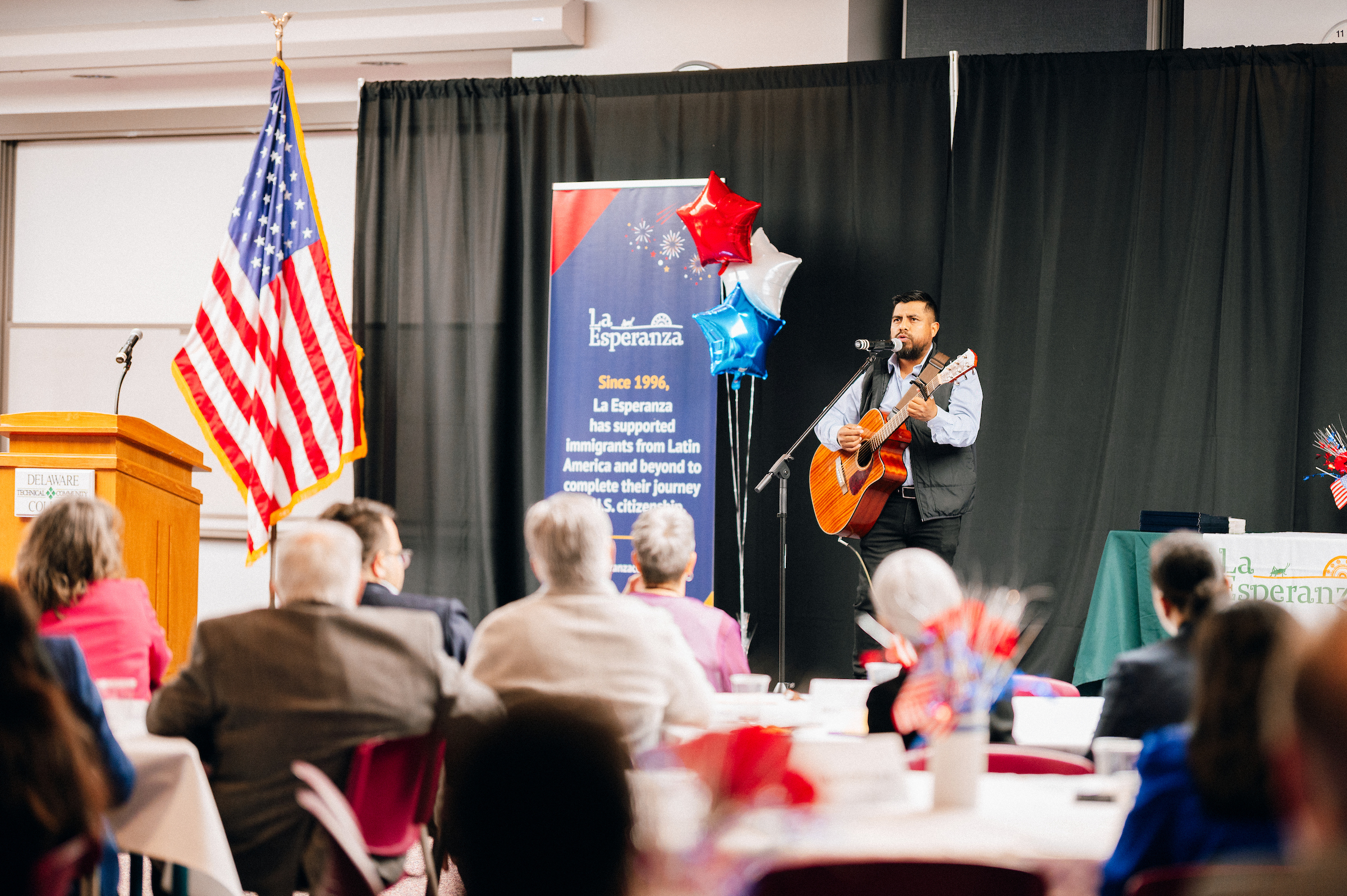 Room with attendees of the 2025 Citizenship Celebration watching a guitarist play